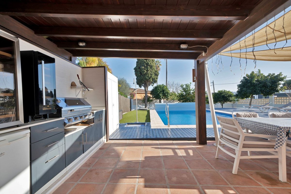 Outdoor kitchen with grill and wine fridge opens to a pool area with lounge chairs and dining table.