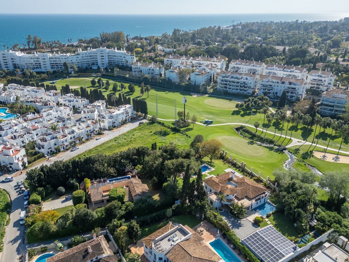 Aerial view of a luxury villa and apartment complex overlooking a golf course with the sea in the background.