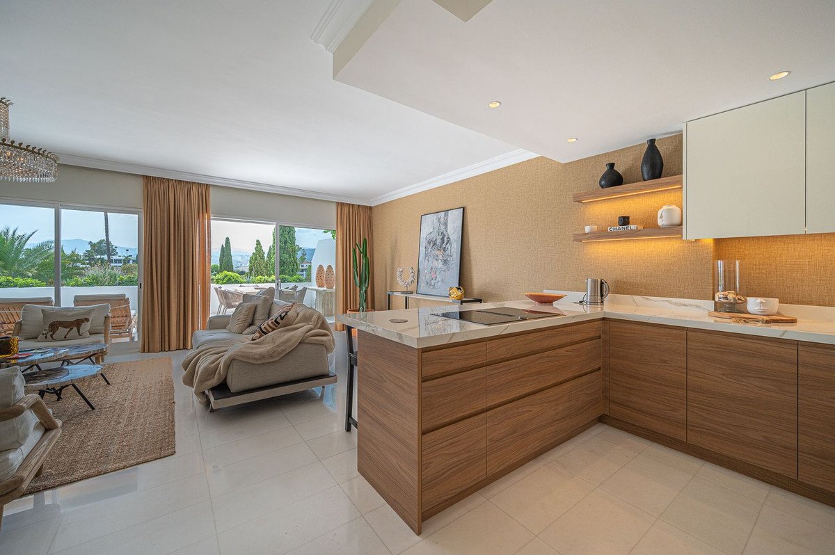 Modern open-plan living room and kitchen with a view of the sea and mountains through large sliding doors.