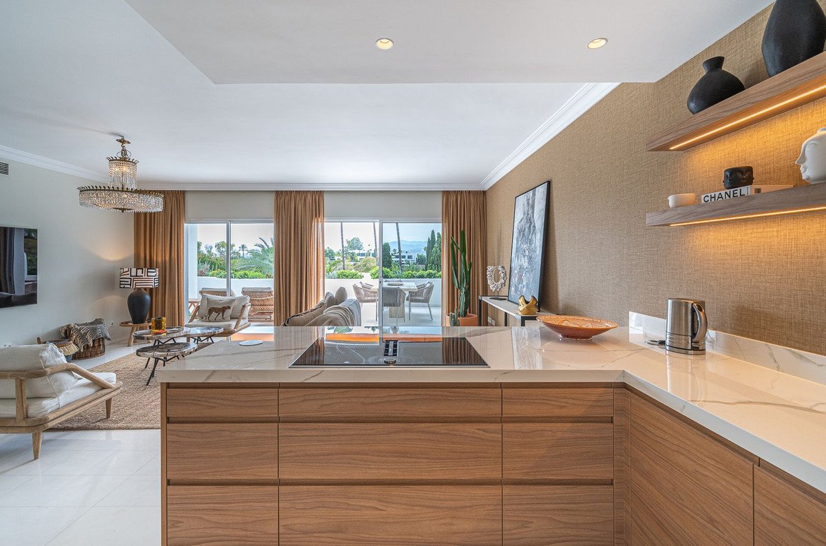 Modern open-concept living area and kitchen with sleek cabinetry, marble countertops, and a view of the sea and greenery.