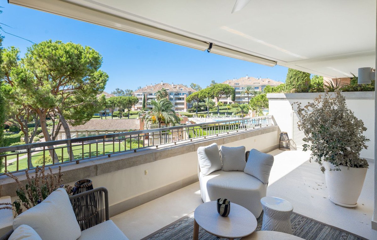 Spacious terrace with comfortable seating, overlooking lush gardens and Mediterranean-style buildings under a clear blue sky.