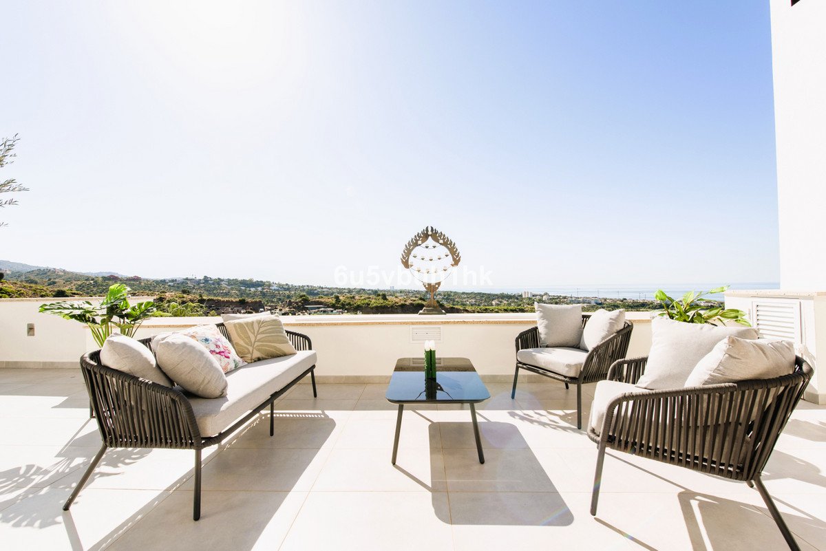 A contemporary outdoor seating area on a spacious terrace with a beautiful sea and landscape view under a clear sky.