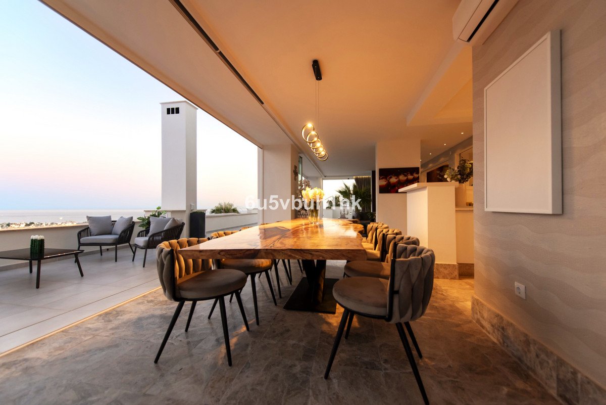 Modern dining area with a long wooden table and plush chairs opening to a terrace with a sea view.