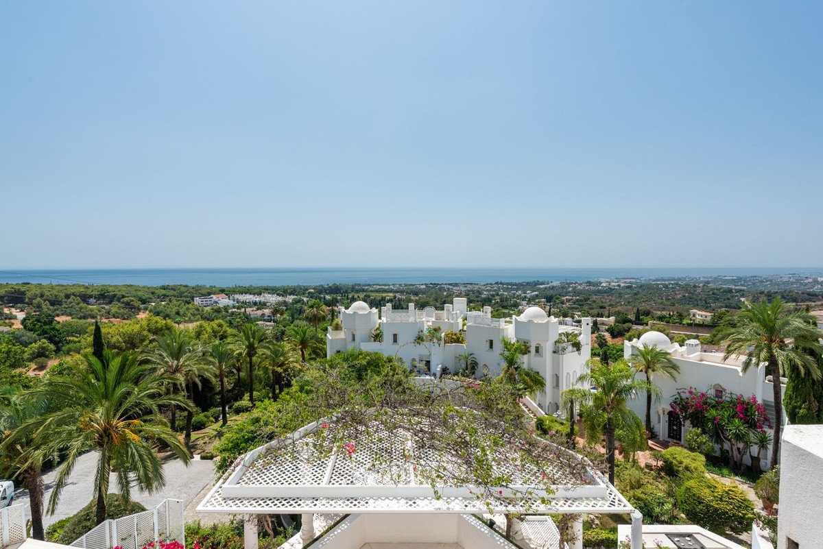 Expansive view of a white villa with lush greenery and a distant sea under a clear blue sky.