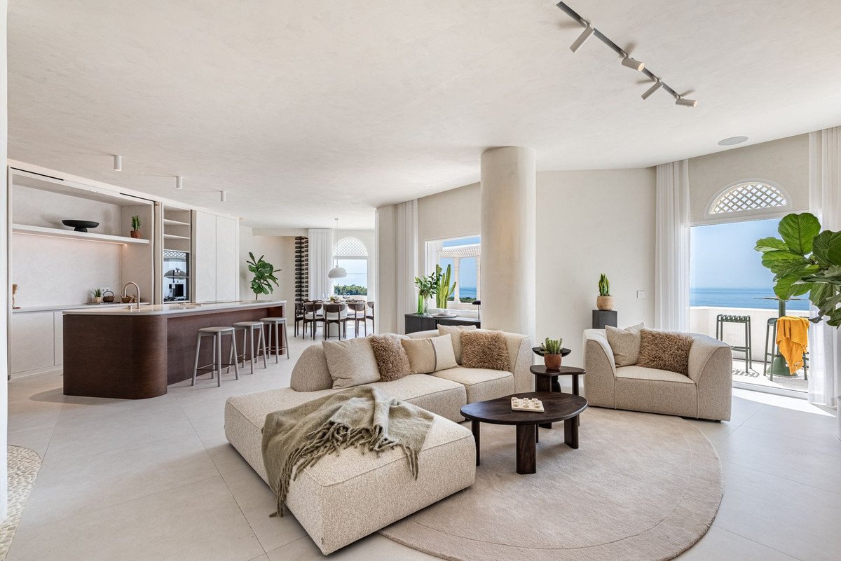 Spacious living and kitchen area with modern furniture, island, and a balcony offering a stunning sea view.