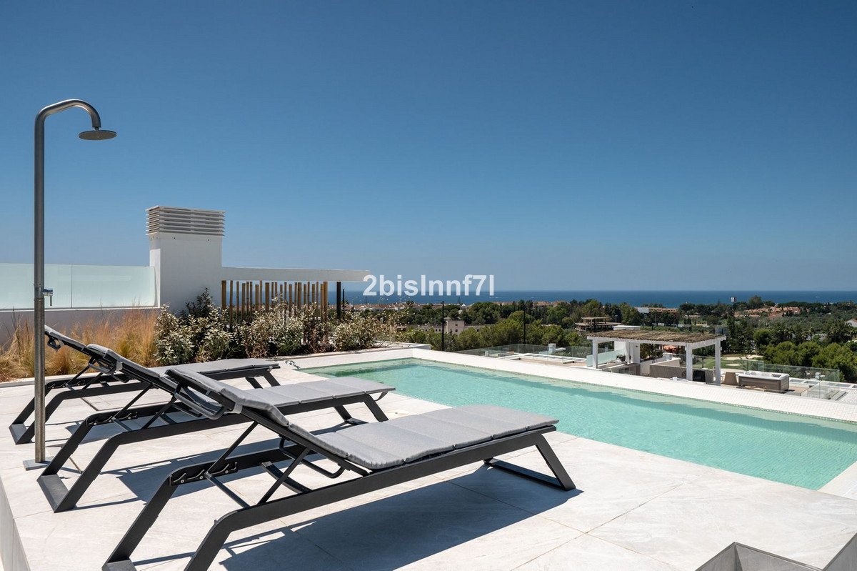 Modern terrace with a swimming pool, lounge chairs, outdoor shower, and a distant sea view on a sunny day.