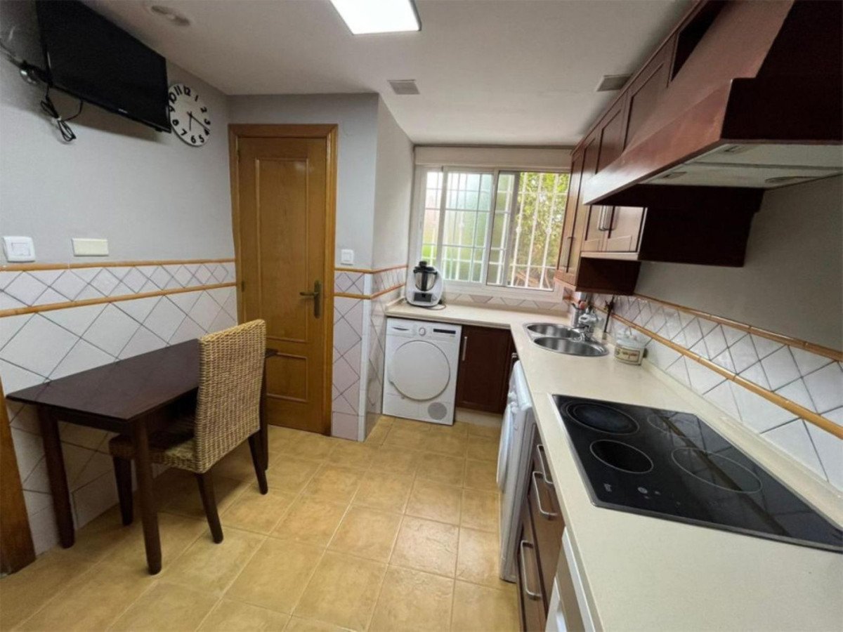 Modern kitchen with white countertops, dark wood cabinets, a washing machine, oven, and a small dining table by the window.