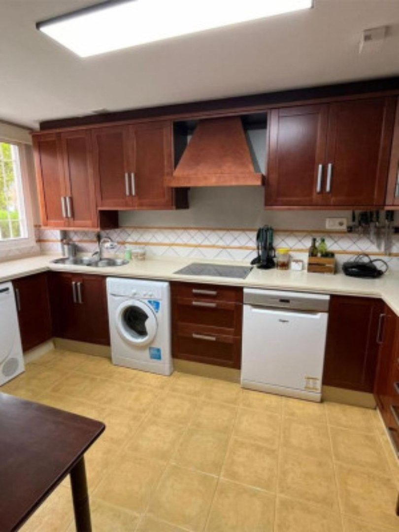 A kitchen with dark wood cabinets, a washing machine, and a dishwasher, featuring a tiled backsplash and countertops.