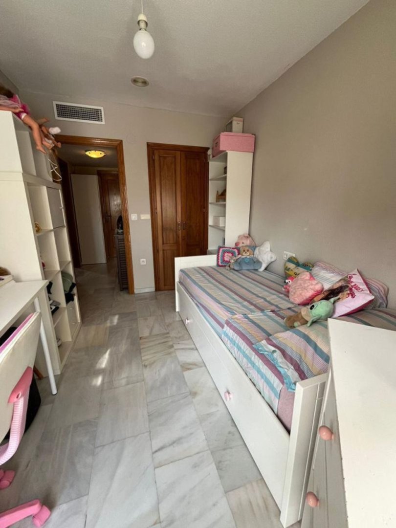 A child's bedroom with a single bed, white shelving, a desk, and marble flooring. Soft toys are on the bed.