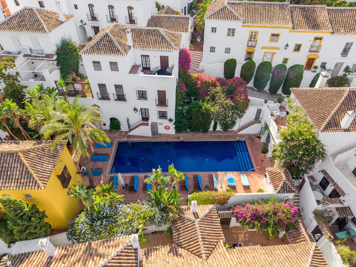 Aerial view of a Mediterranean villa complex featuring a large blue swimming pool surrounded by lush gardens and white buildings.