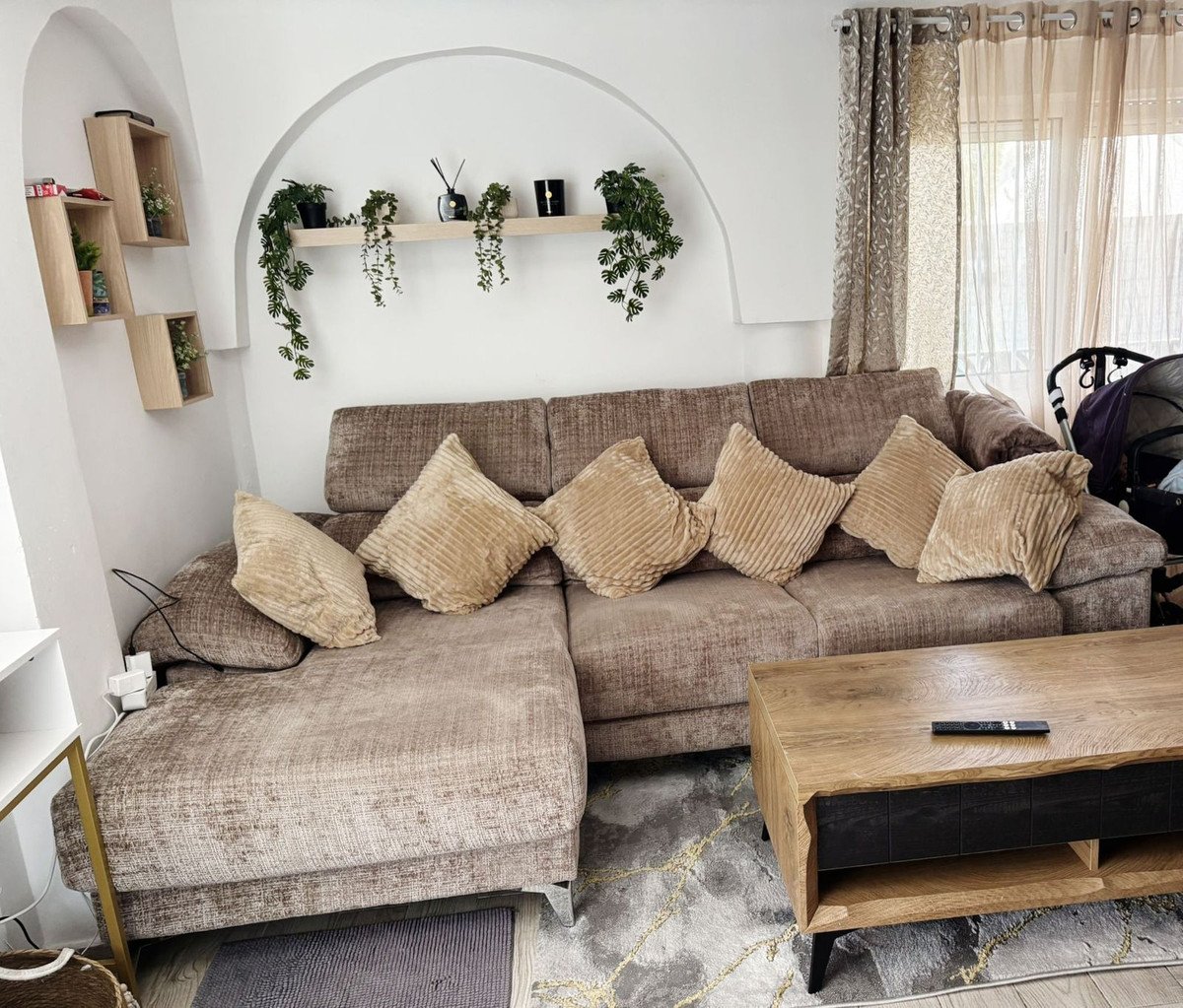 A sectional sofa with plush cushions, a wooden coffee table, and decorative plants on shelves in a living room.