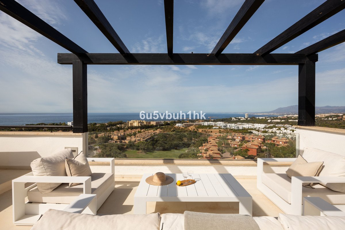 Modern white outdoor lounge furniture on a terrace with sea and resort views under a wooden pergola.