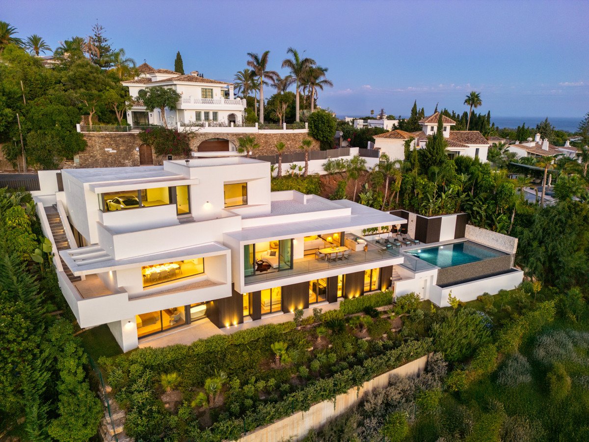 Modern villa with infinity pool, terrace, and sea views, surrounded by lush greenery.