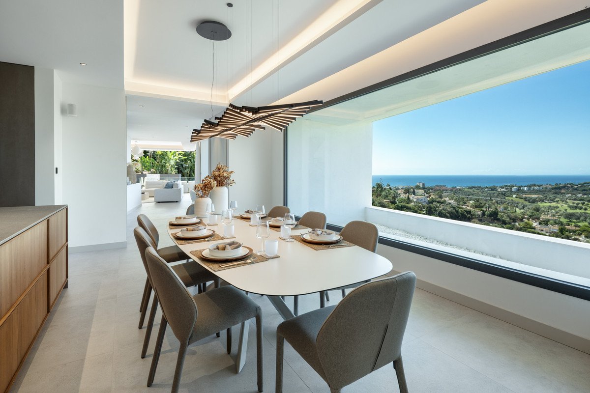 Elegant dining area with a large window showcasing a breathtaking ocean and landscape view. Modern chandelier above the chandelier above the table.