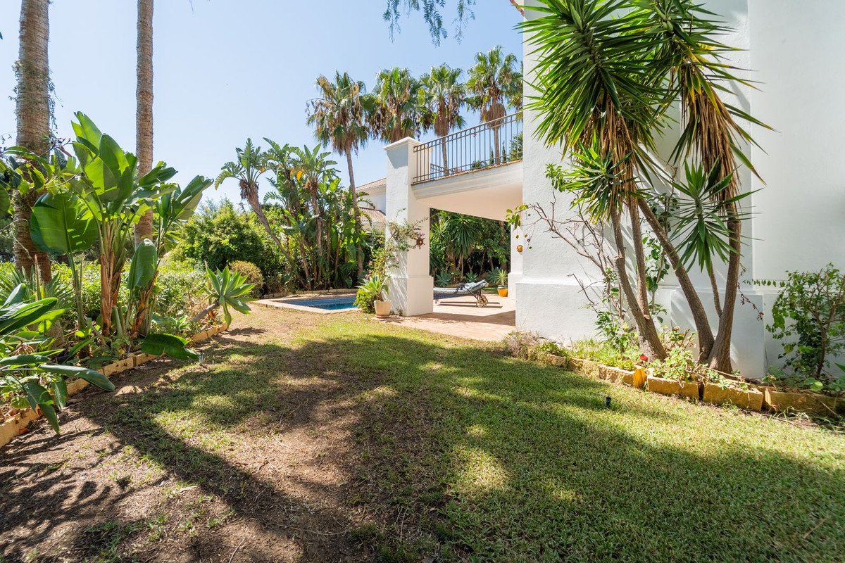 Lush tropical garden with a swimming pool, green lawn, and a white building with a balcony on a sunny day.
