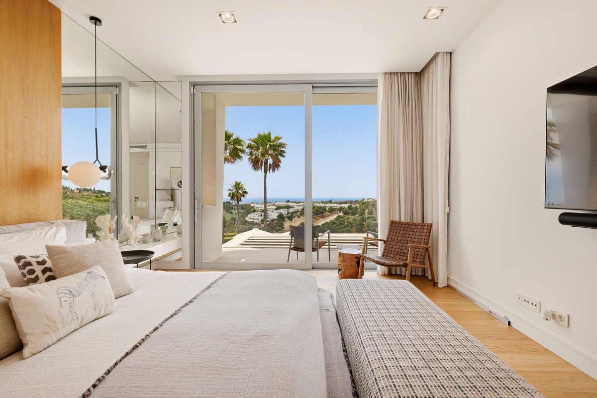 Spacious bedroom with a king-size bed and sliding glass doors opening to a balcony with sea and palm tree views.