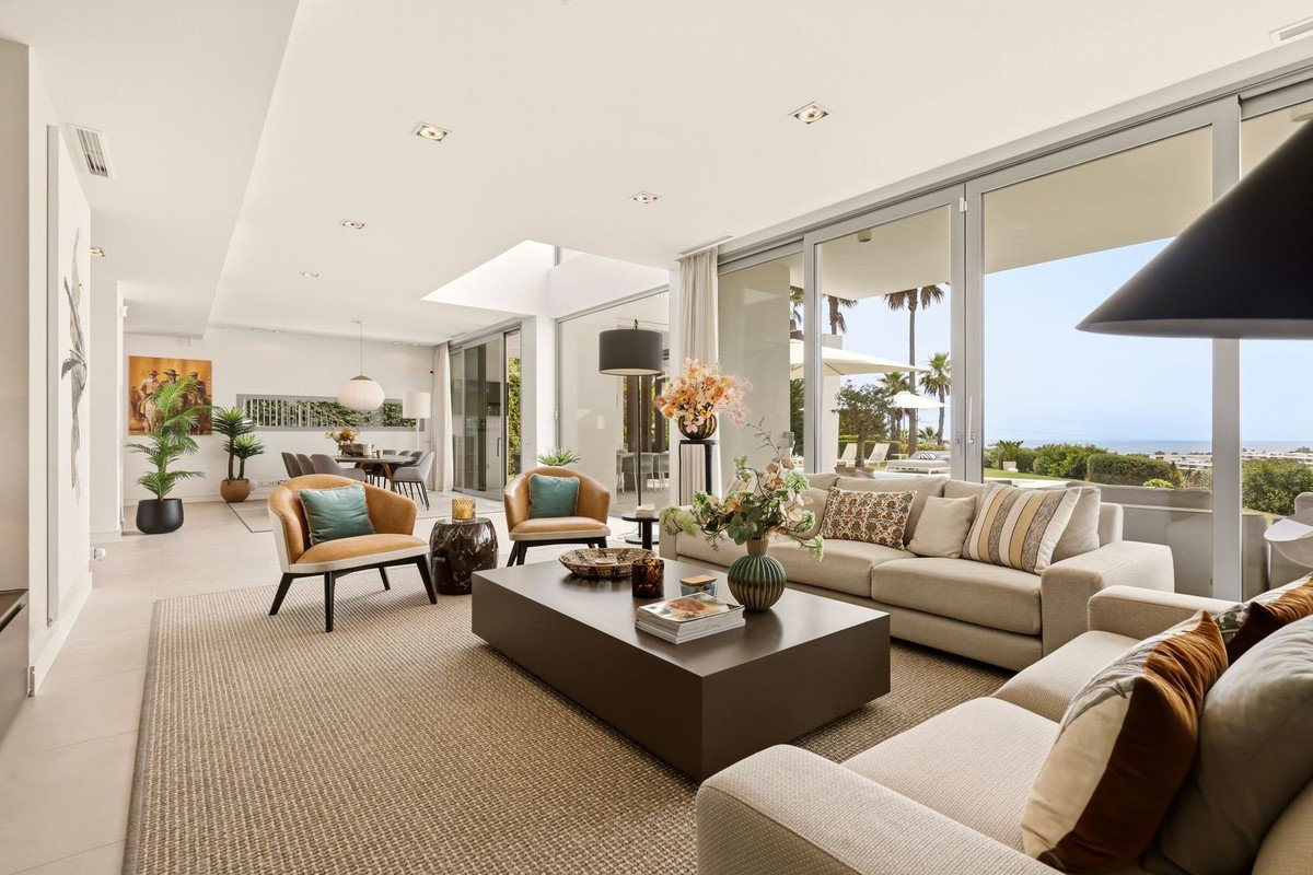 Spacious modern living room with comfortable sofas, armchairs, and a large coffee table, offering a beautiful sea view through glass doors.
