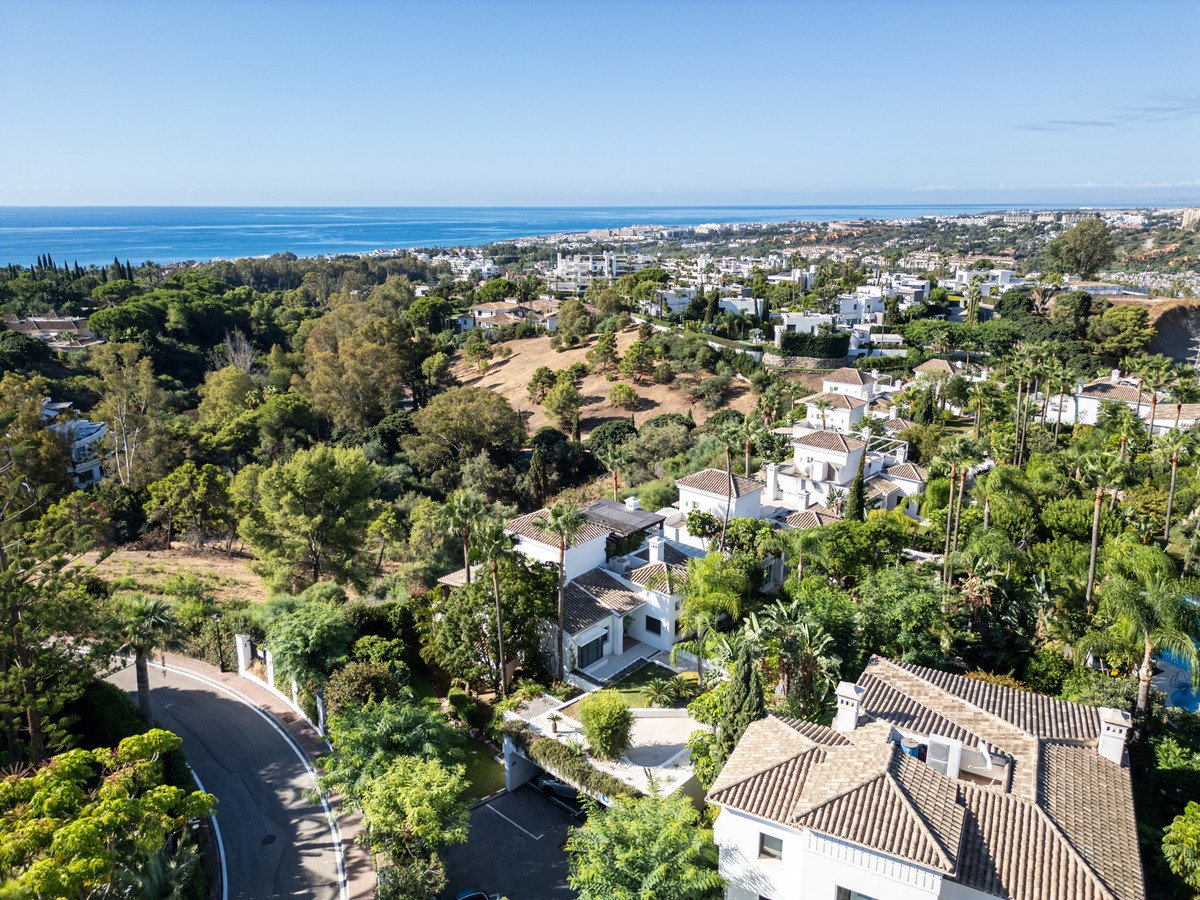 Aerial view of modern villas nestled in lush greenery with the sea and coastline in the background on a sunny day.
