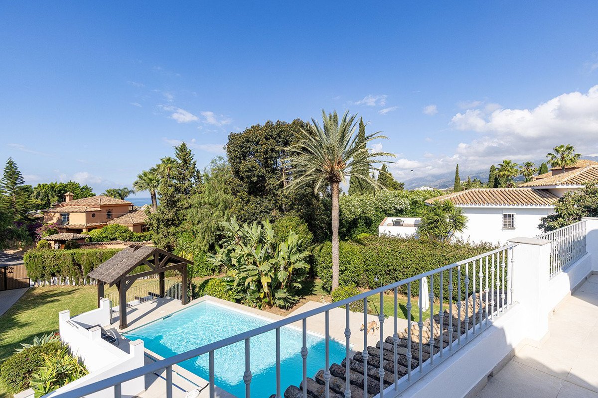 Villa with pool, palm trees, and sea view under blue sky.