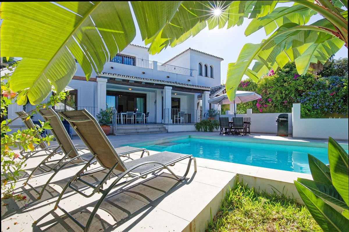 Luxurious two-story house with a swimming pool and lounge chairs surrounded by lush greenery