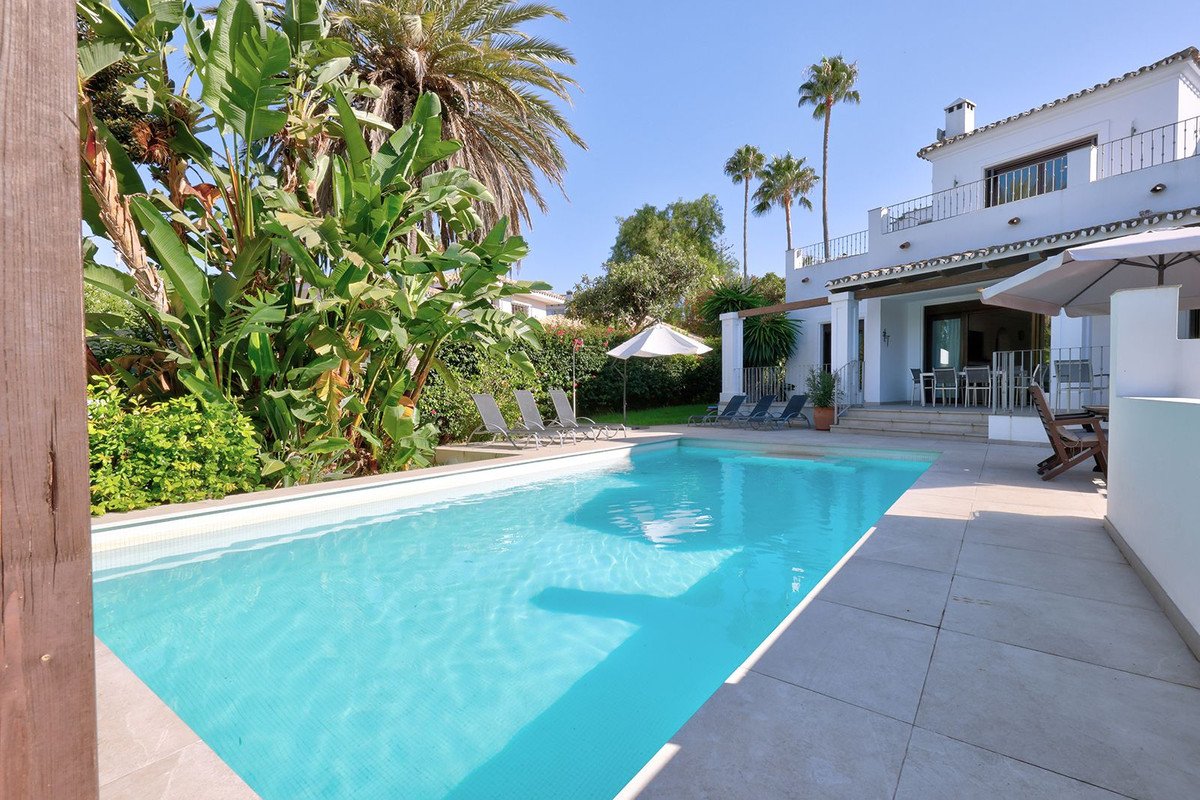 Swimming pool with white house and lush garden, sunny outdoor area