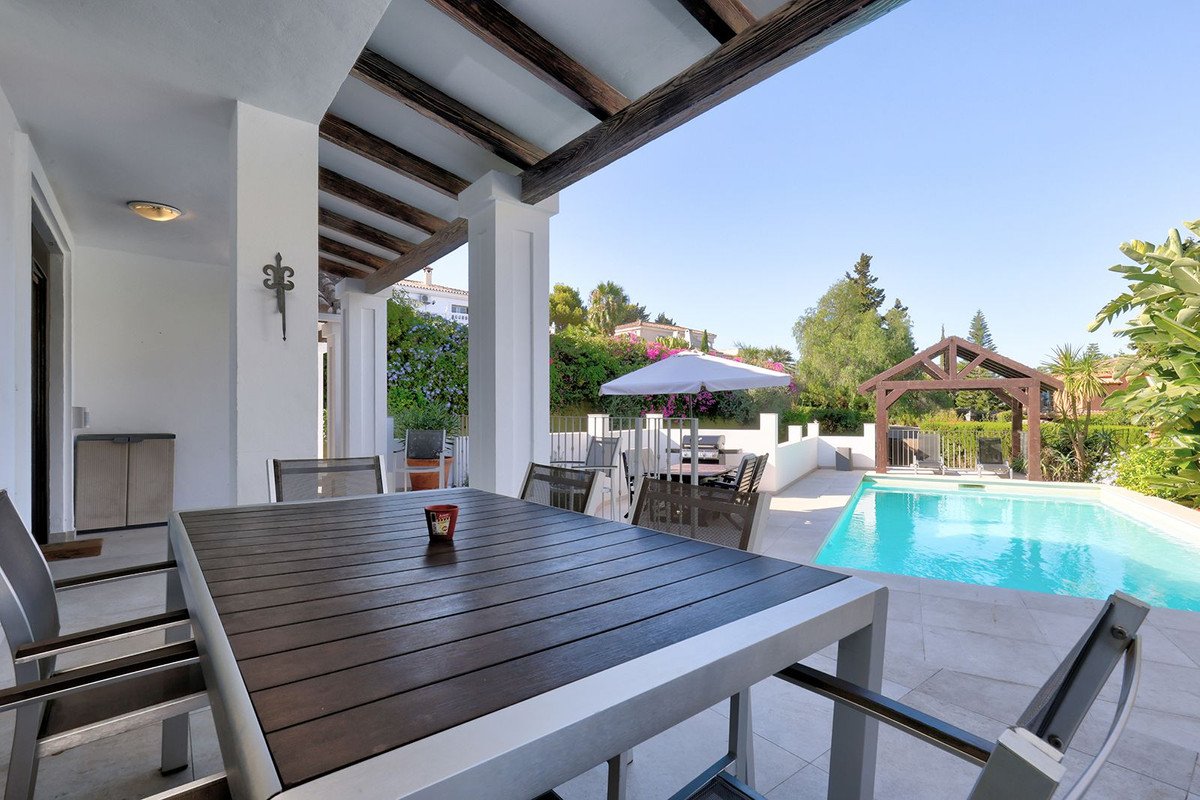 Covered outdoor dining area with a swimming pool and garden view