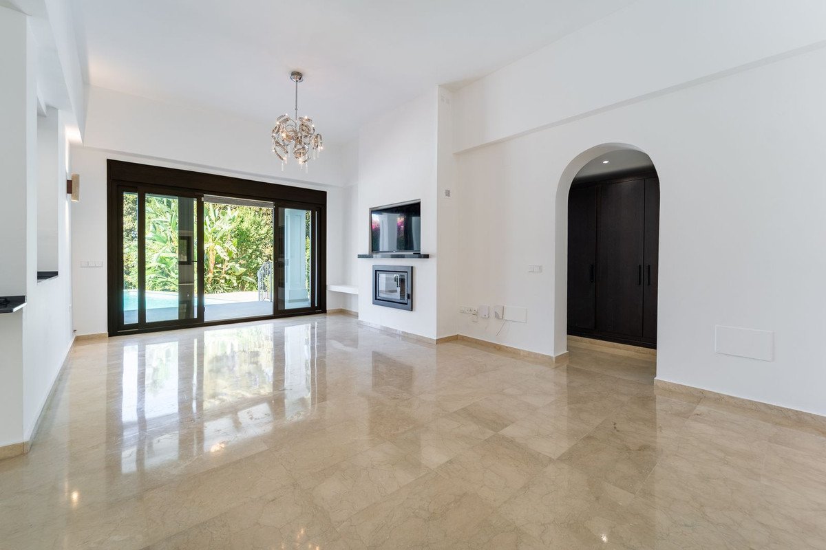 Modern living room with fireplace, TV, and large sliding doors opening to a pool and lush garden view.