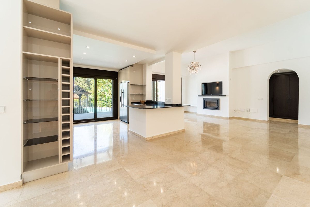 Spacious modern living area with kitchen island, fireplace, TV, and sliding doors revealing a garden and pool view.