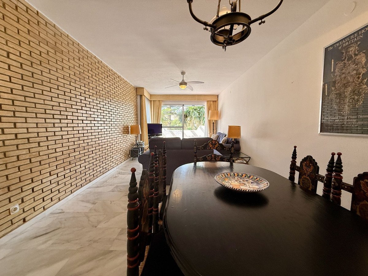 Spacious living and dining area with a textured brick wall, a dark wood dining set, and views of greenery through the window.