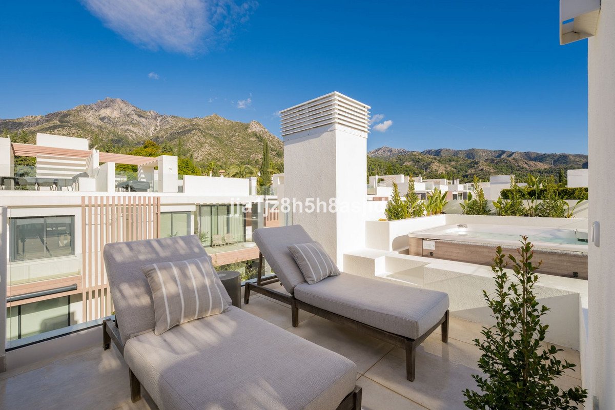 A modern terrace with two lounge chairs, a jacuzzi, and a stunning mountain view under a clear blue sky.
