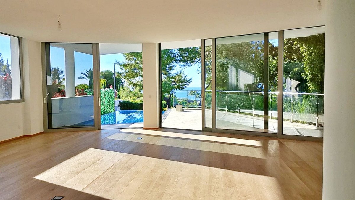 Spacious living room with large windows overlooking ocean, pool, and garden.