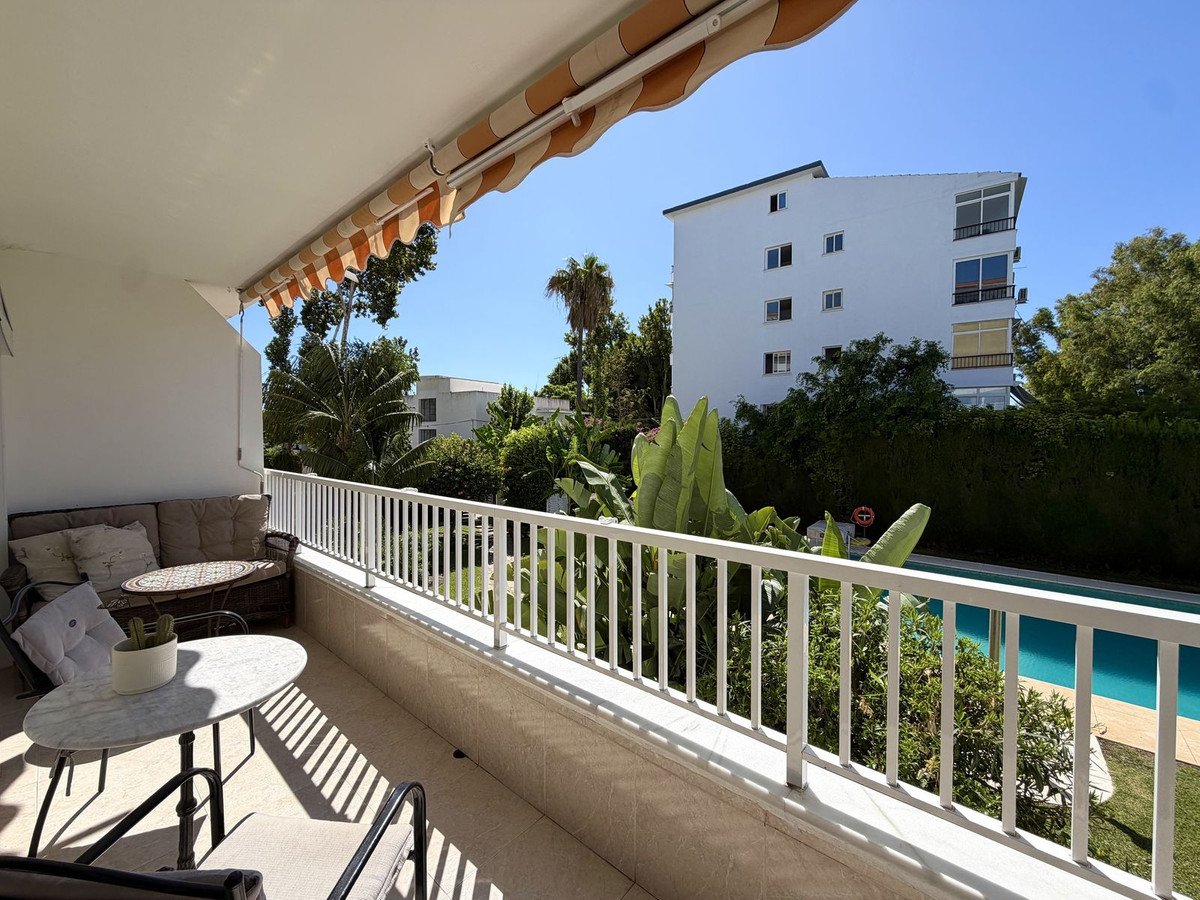 A balcony with outdoor seating, overlooking a swimming pool surrounded by lush greenery and a modern building.