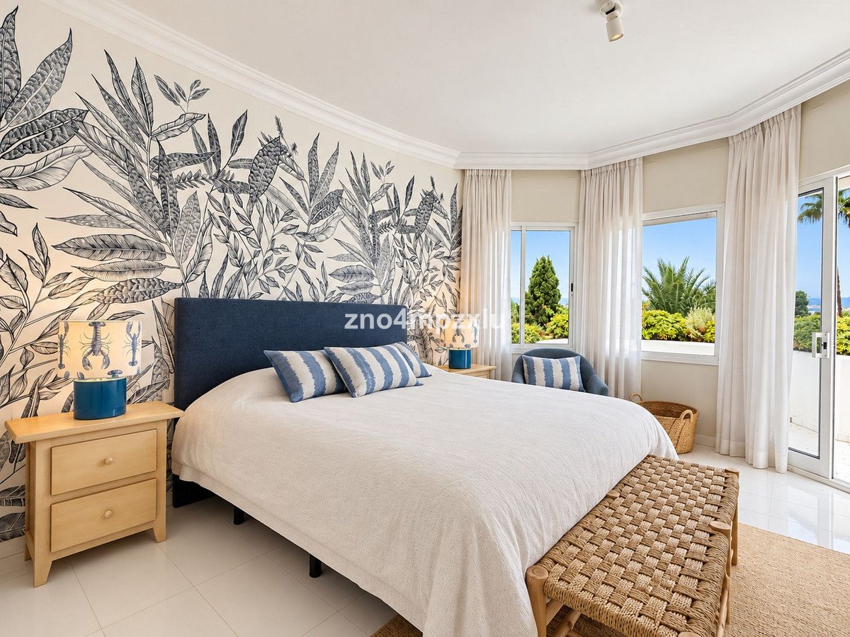 Bedroom with botanical wallpaper, large bed, ocean view through windows, and a balcony.