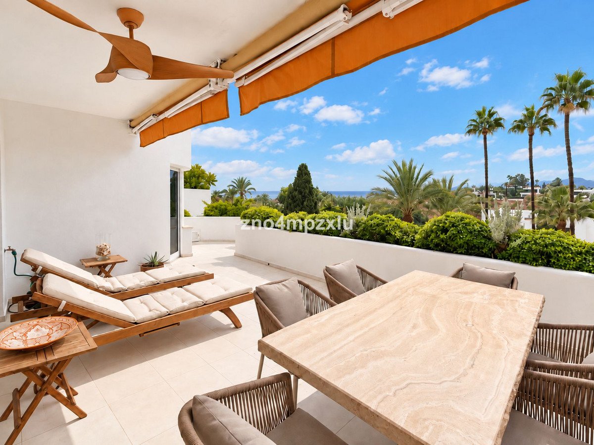 Spacious terrace with lounge chairs, dining table, and lush green vegetation overlooking the sea under a blue sky.
