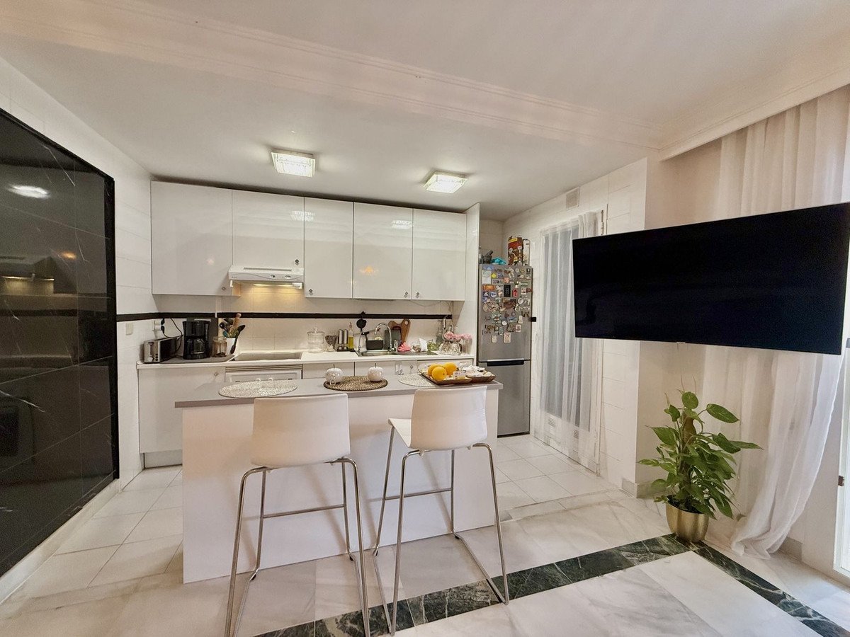 Modern kitchen with white cabinets, island, stools, and a mounted TV.
