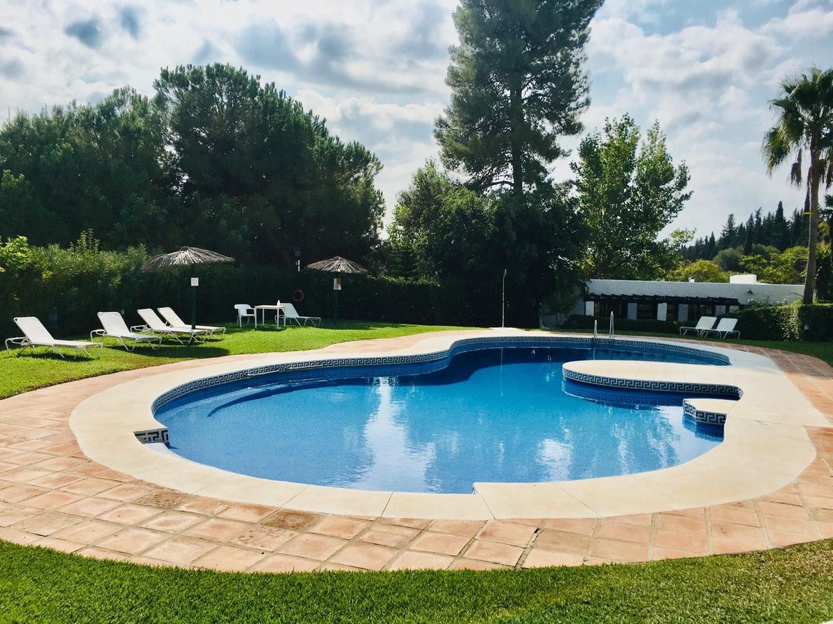 A kidney-shaped swimming pool with blue tiled water, surrounded by a paved deck and lounge chairs on a grassy area.