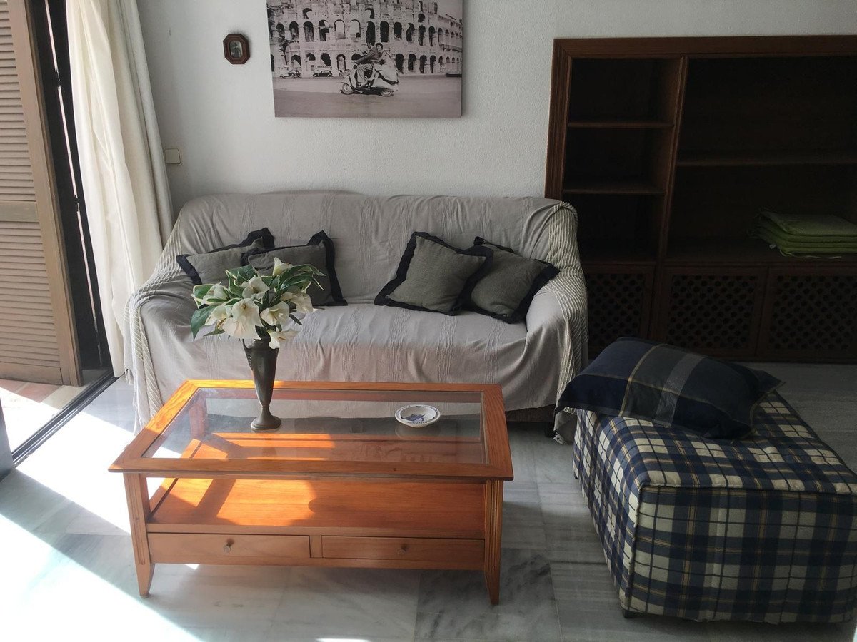 Living room with a comfortable sofa, glass-top coffee table, patterned ottoman, and a large wooden bookshelf.