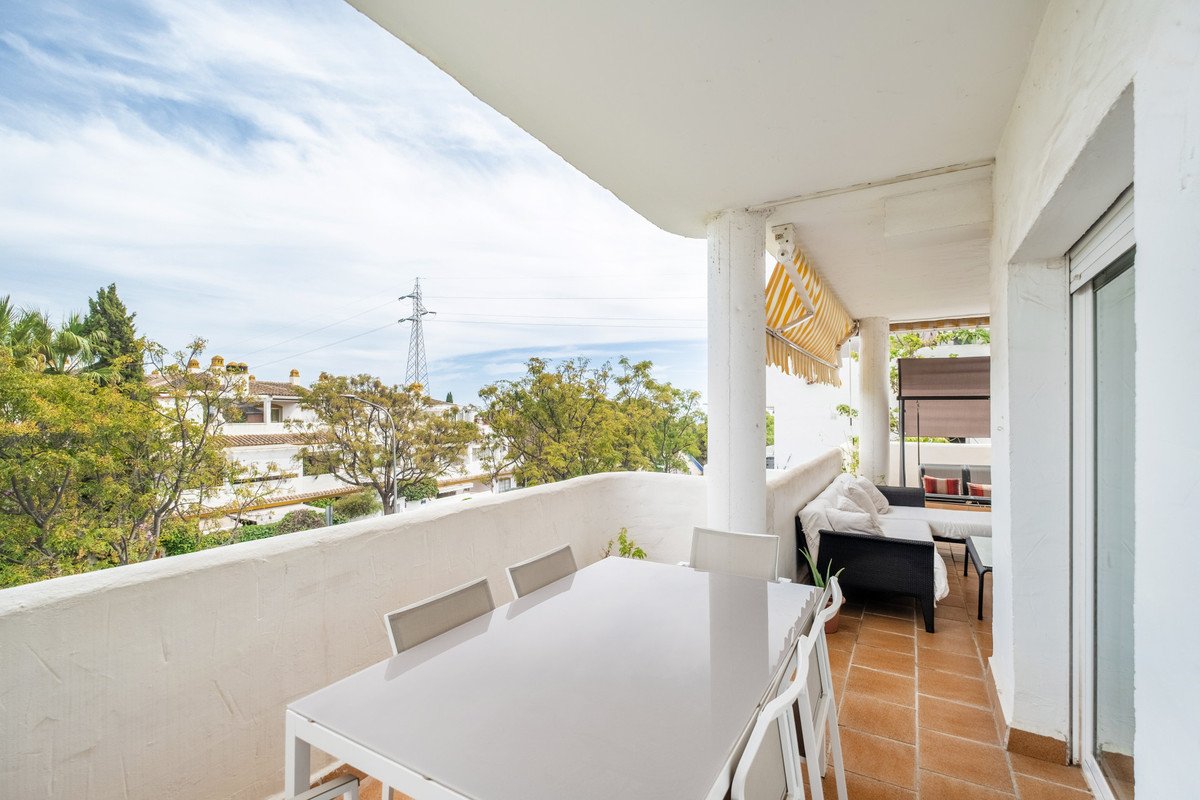 A spacious terrace with dining table and chairs, lounge seating, and a view of trees and buildings under a cloudy sky.