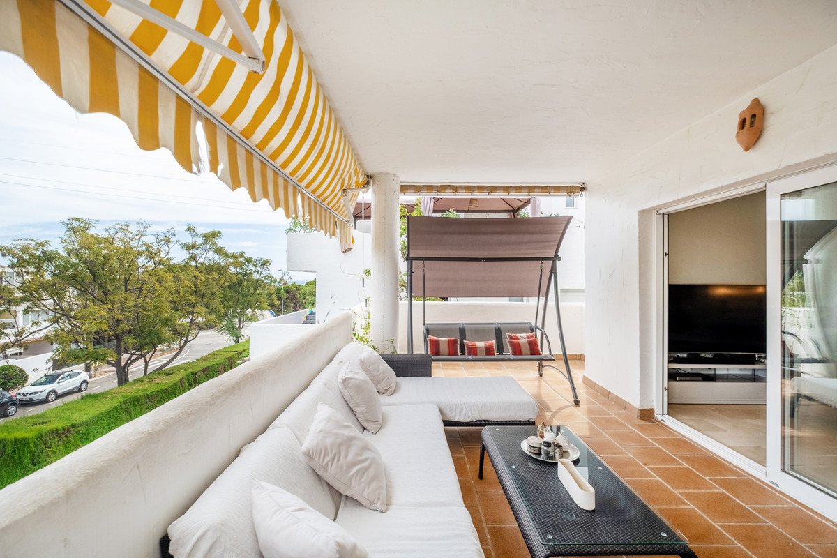 Spacious terrace with a sectional sofa, coffee table, swing, and view of trees and a street.
