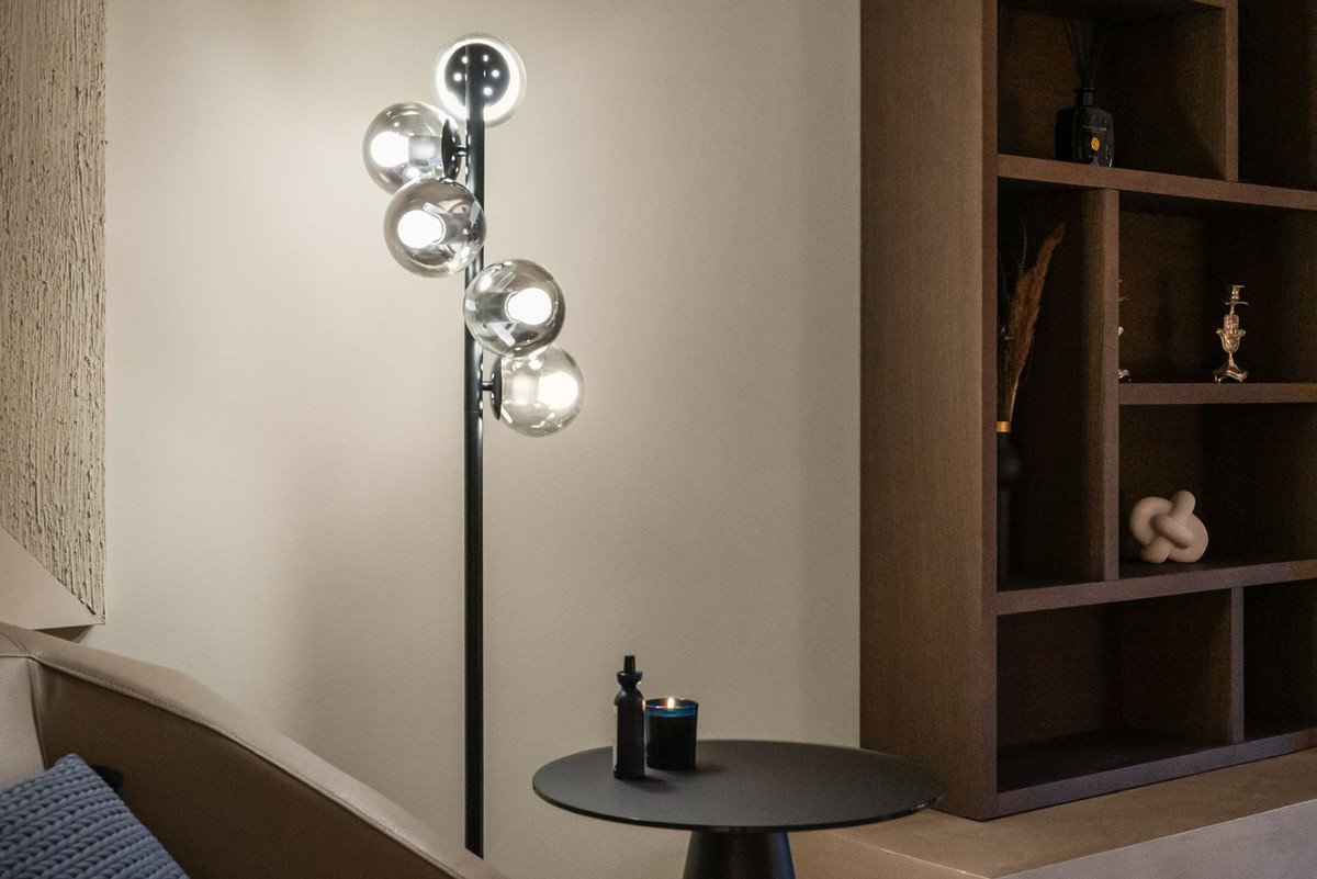 A modern floor lamp with multiple glass globes illuminates a stylish living room corner with shelves and a small table.