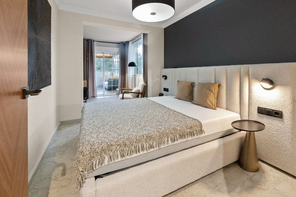 Modern bedroom with large bed, textured headboard, and balcony access with outdoor seating visible.