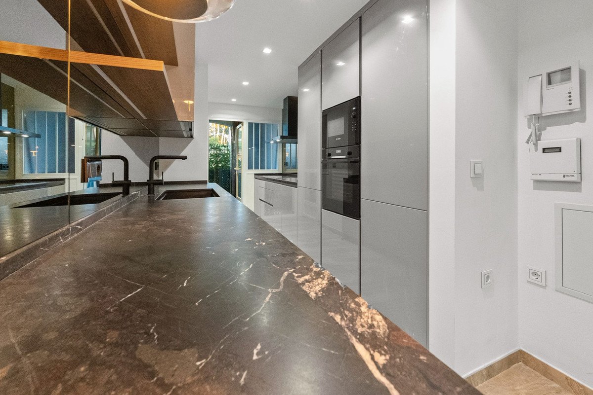 Modern kitchen with sleek grey cabinets, built-in oven, a marble countertop with a double sink, and a door leading outdoors.