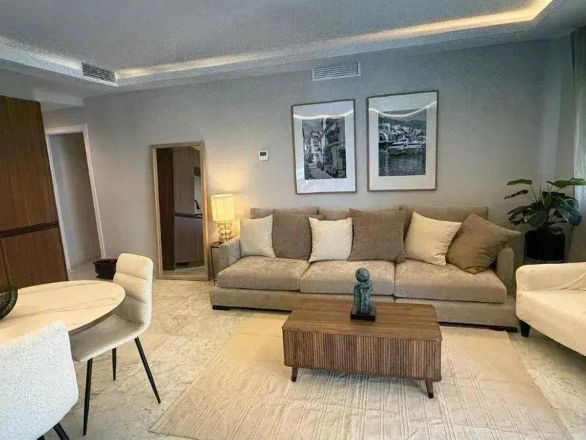 Modern living room with a large sofa, artwork on the wall, a coffee table, and a dining area.