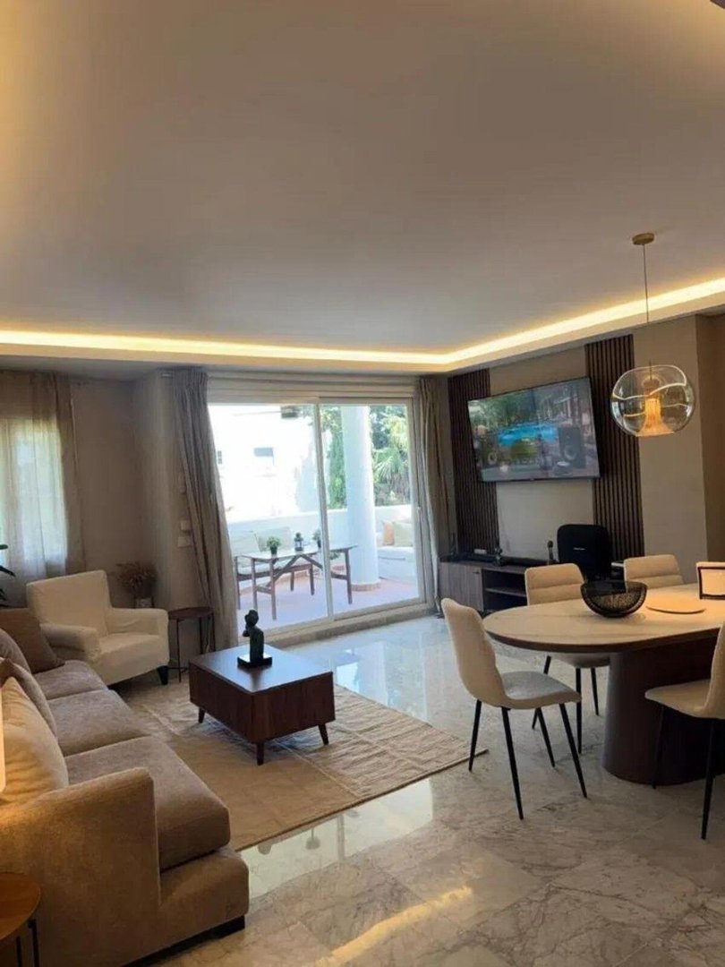 Modern living and dining area with balcony access, featuring a sofa, dining table, and television.