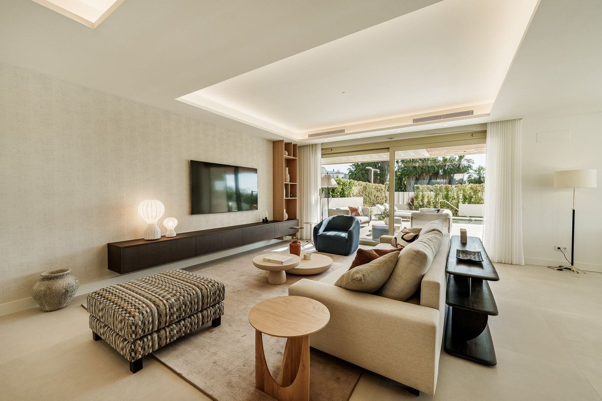 Modern living room with a large sofa, armchair, and coffee tables, leading to a terrace with outdoor seating and lush greenery.