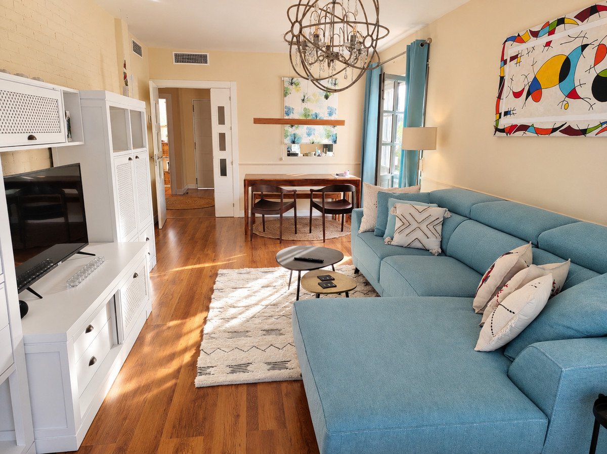 Living room with blue sofa, wooden flooring, and dining area in background