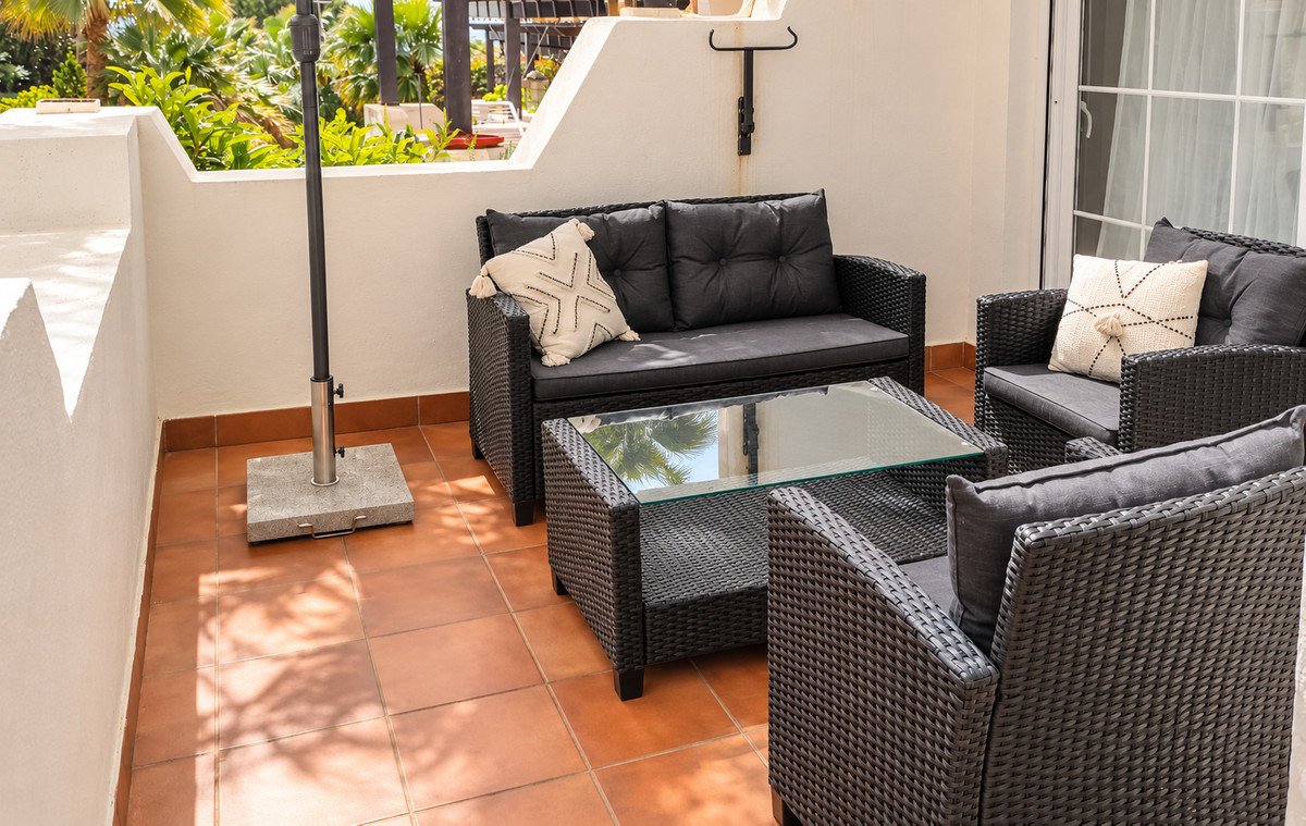 Outdoor patio with wicker furniture, glass table, and tropical garden view