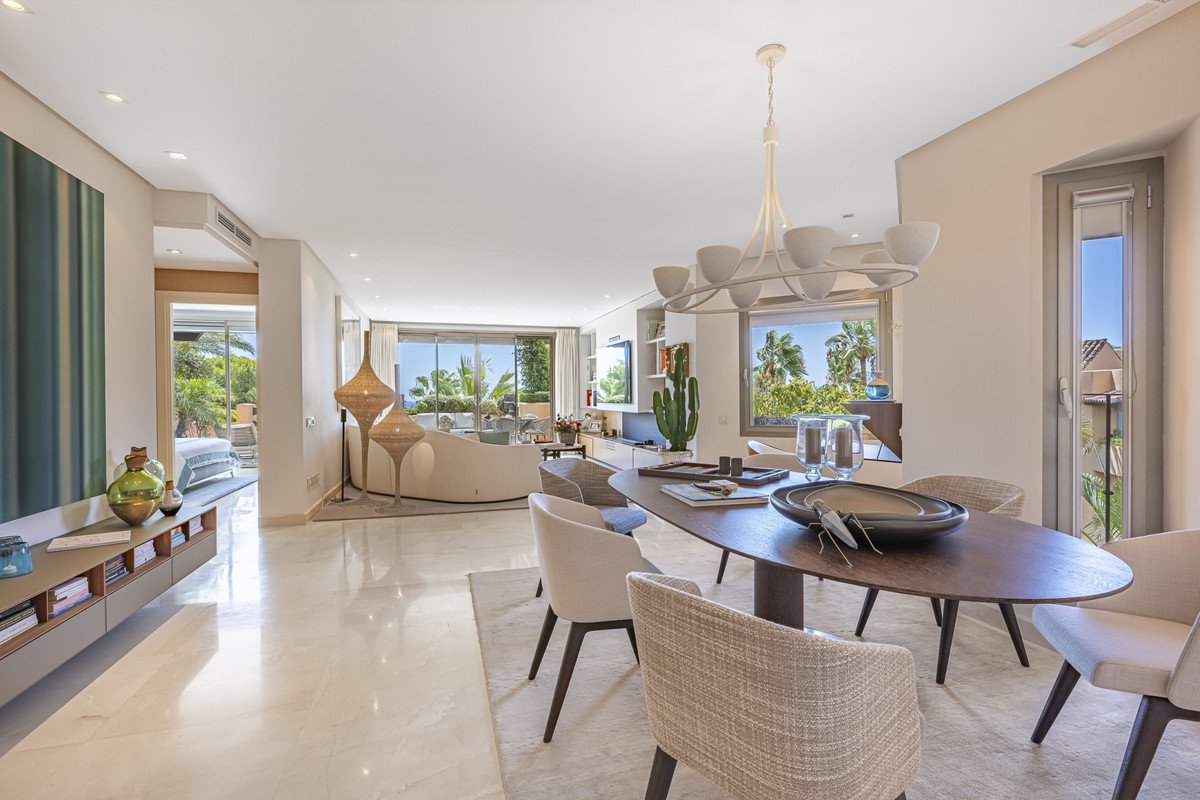 Spacious open-plan living and dining area with a modern sofa, elegant table, and a view of palm trees and the sea.