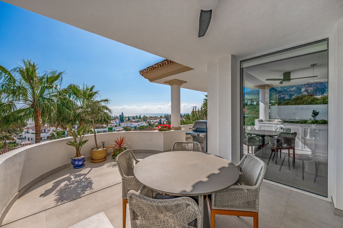 Spacious terrace with dining set and barbecue overlooking a town and the sea under a clear blue sky.