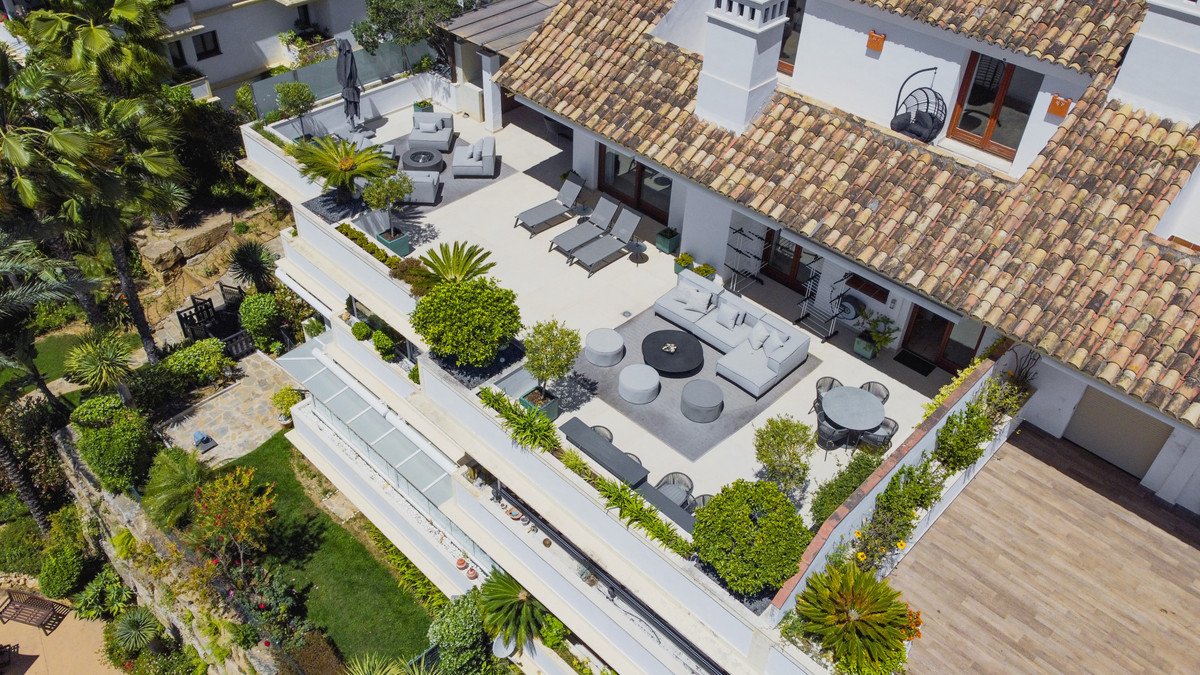 Spacious outdoor terrace with lounge furniture, dining area, sunbeds, and lush greenery, offering a scenic view.